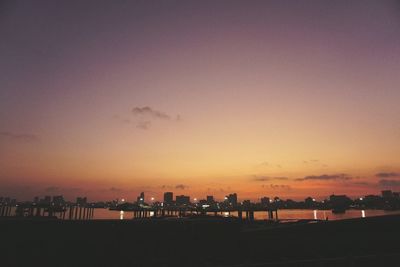 Silhouette city by sea against sky during sunset