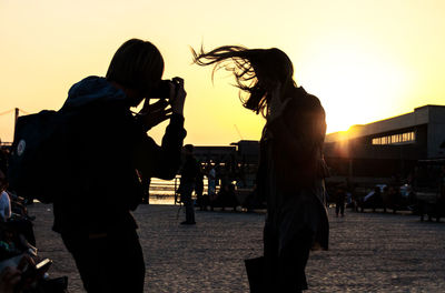 Silhouette people on sidewalk against sky during sunset