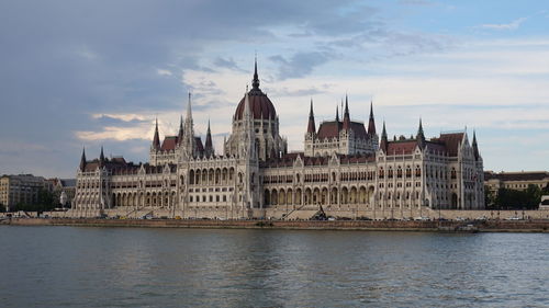 View of buildings by river against cloudy sky