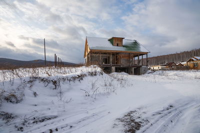 A dacha under construction stands on a hillock on the outskirts of the village in winter.