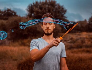 Portrait of man holding bubble wand on field