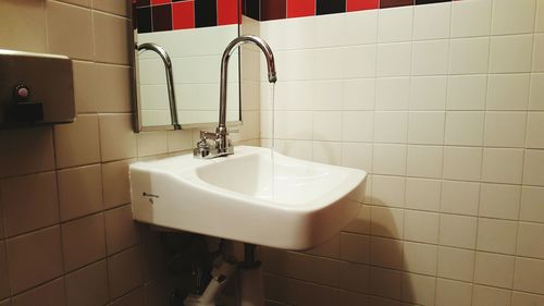 Water running from bathroom sink faucet against tiled wall