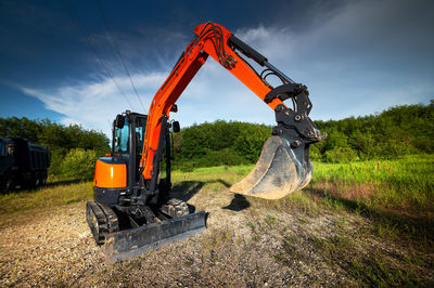 Bulldozer stands on a piece of land against the backdrop of a bright blue sky and green trees