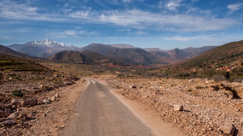 Dirt road along landscape and mountains against sky