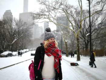 Woman wearing warm clothing while standing on snow covered footpath in city