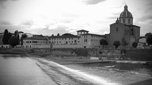 View of buildings by river against cloudy sky