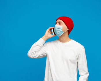 Man wearing mask talking on phone standing against blue background