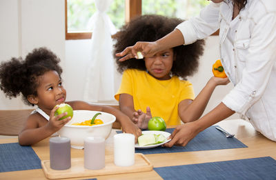 Midsection of woman by daughters with breakfast on table