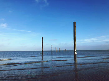 Wooden posts in sea against blue sky