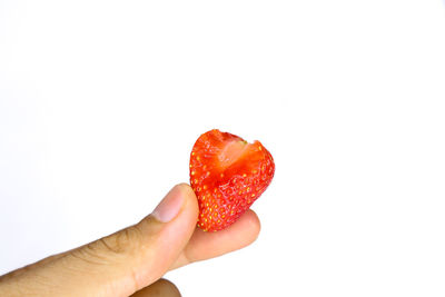 Close-up of hand holding strawberry over white background