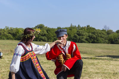 Portrait of man in traditional clothing kissing hand of woman while kneeling on field 