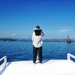 Rear view of woman standing on boat in sea against blue sky