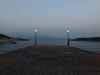 Street lights on pier by sea against sky