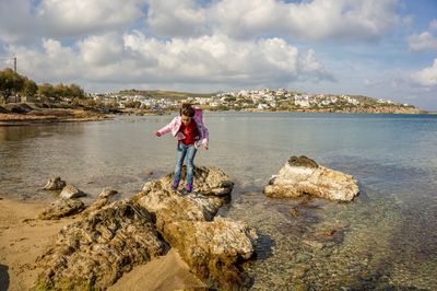 Woman standing on rock by sea against sky