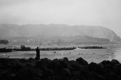 Silhouette man fishing by sea against clear sky