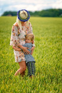 Mother with son standing on agricultural field against sky