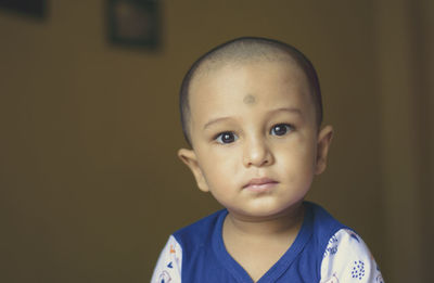 Cute bald indian baby boy in blue and white shirt looking away. head and shoulder shot. close up.