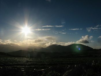Sun shining on field against sky during sunset