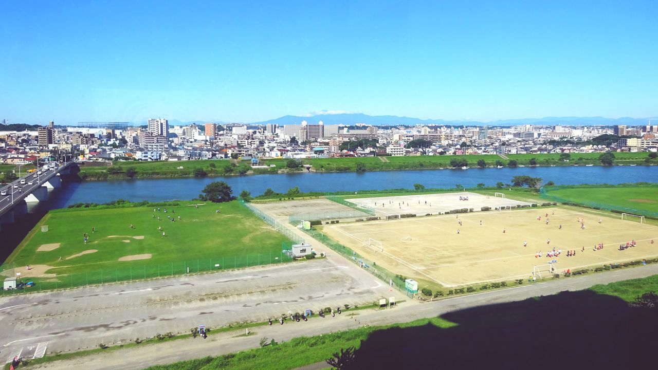 architecture, building exterior, built structure, grass, clear sky, copy space, city, cityscape, blue, high angle view, landscape, green color, travel destinations, large group of people, water, tourism, lawn, outdoors, incidental people, day