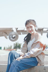 Portrait of smiling young woman sitting against sky