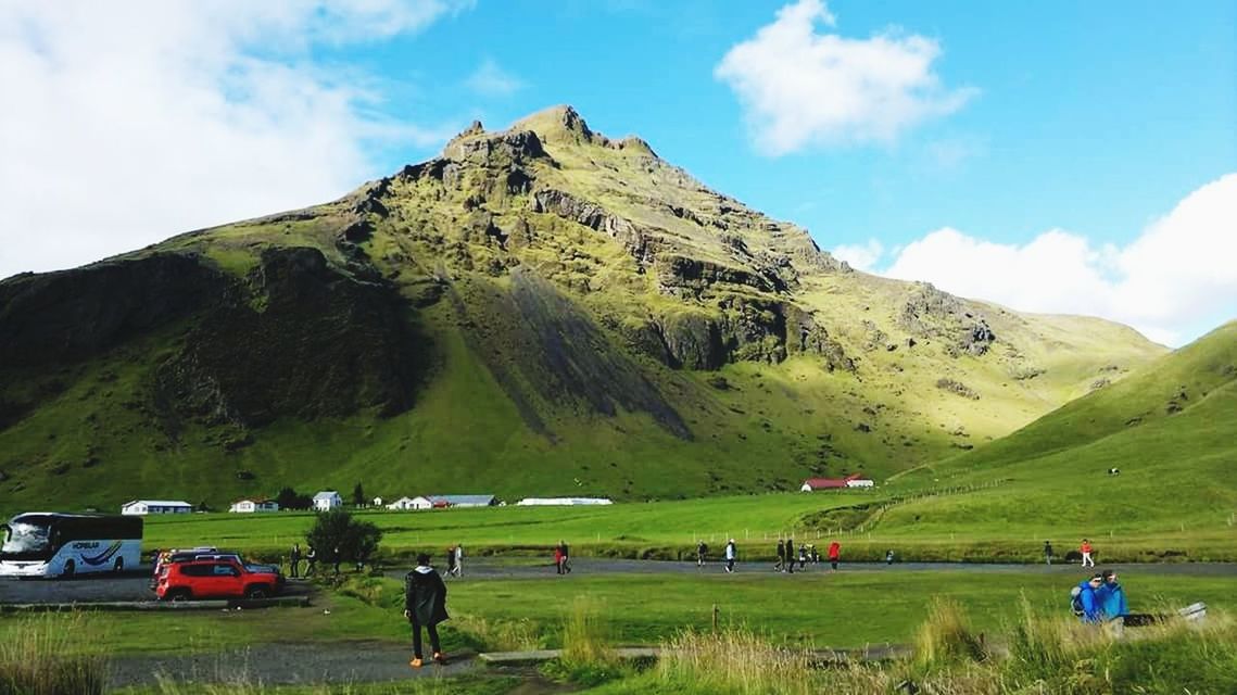 mountain, sky, green color, nature, grass, scenics, cloud - sky, beauty in nature, day, landscape, road, land vehicle, car, growth, real people, transportation, field, tranquil scene, outdoors, tranquility, mountain range, men, tree, people