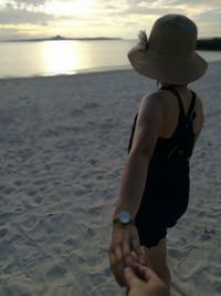 Cropped image of hand holding woman at beach against sky during sunset