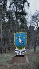 Information sign by bare trees in forest against sky