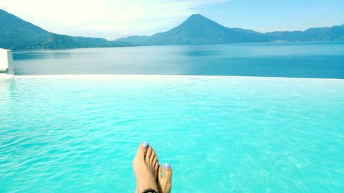 Low section of woman relaxing on blue sea against sky