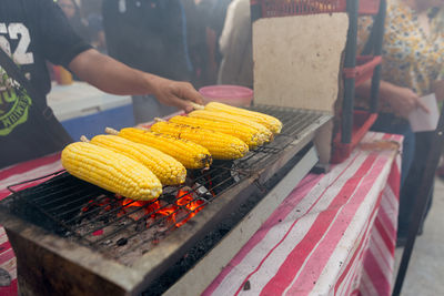 Close-up of man roasting corn on barbecue grill at market