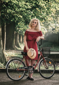 Portrait of woman with bicycle standing against tree