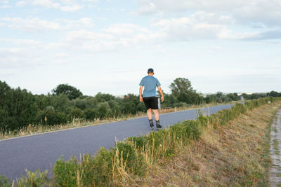 Rear view of man roller skating on road amidst land against sky