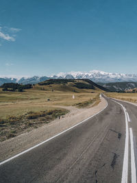 Country road by landscape against sky