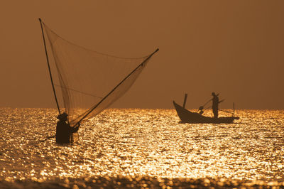 Silhouette fishing boat sailing in sea against orange sky