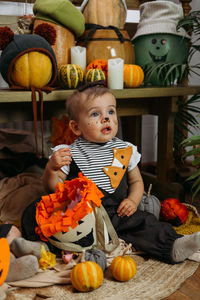 Cute little baby girl dressed in halloween costume sitting on bed with halloween decoration at home