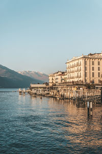 Buildings by sea against clear blue sky