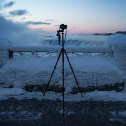 Camera by snow covered railing against waterfall