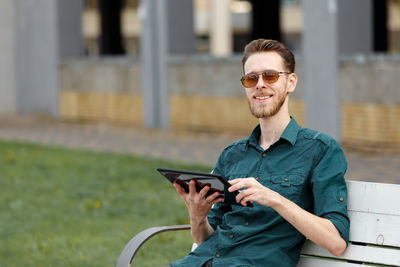 A young man in sunglasses holds a tablet in his hands, reads information on the tablet