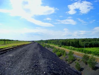 Railroad track on slag by field against sky