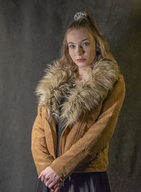 Portrait of young woman standing against black background