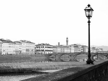 Street light by river against buildings in city against clear sky