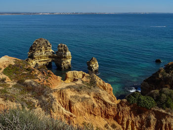 Scenic view of cliff by sea against blue sky