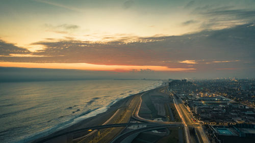 Aerial view of city by sea against sky during sunset