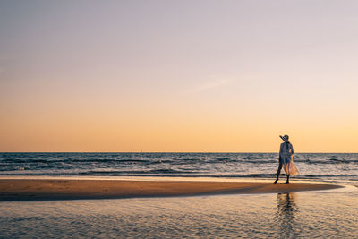 Rear view of woman standing at beach against sky during sunset