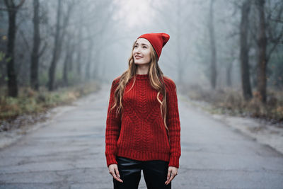 Woman in red hat and sweater walking on foggy mystical morning forest.