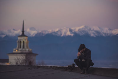 Man smoking while sitting against snowcapped mountain during sunset