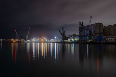 Illuminated pier by sea against sky at night