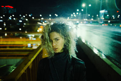 Portrait of young woman standing against illuminated string lights at night