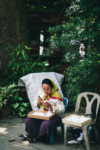 Young woman sitting on book by plants