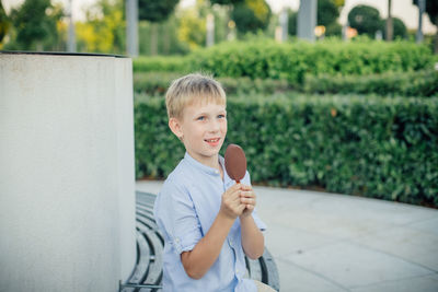 Portrait of boy holding camera while standing outdoors