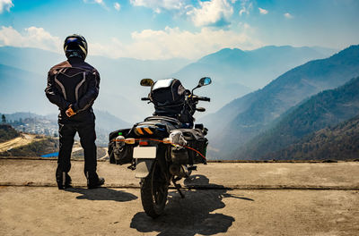 Man motorcyclist watching valley from hill top with his loaded motorcycle and pristine natural view